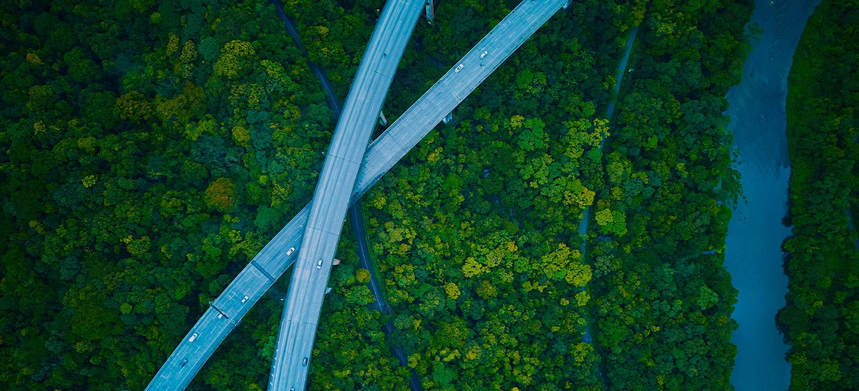 An aerial view of two highways intersect over a green forest and river.