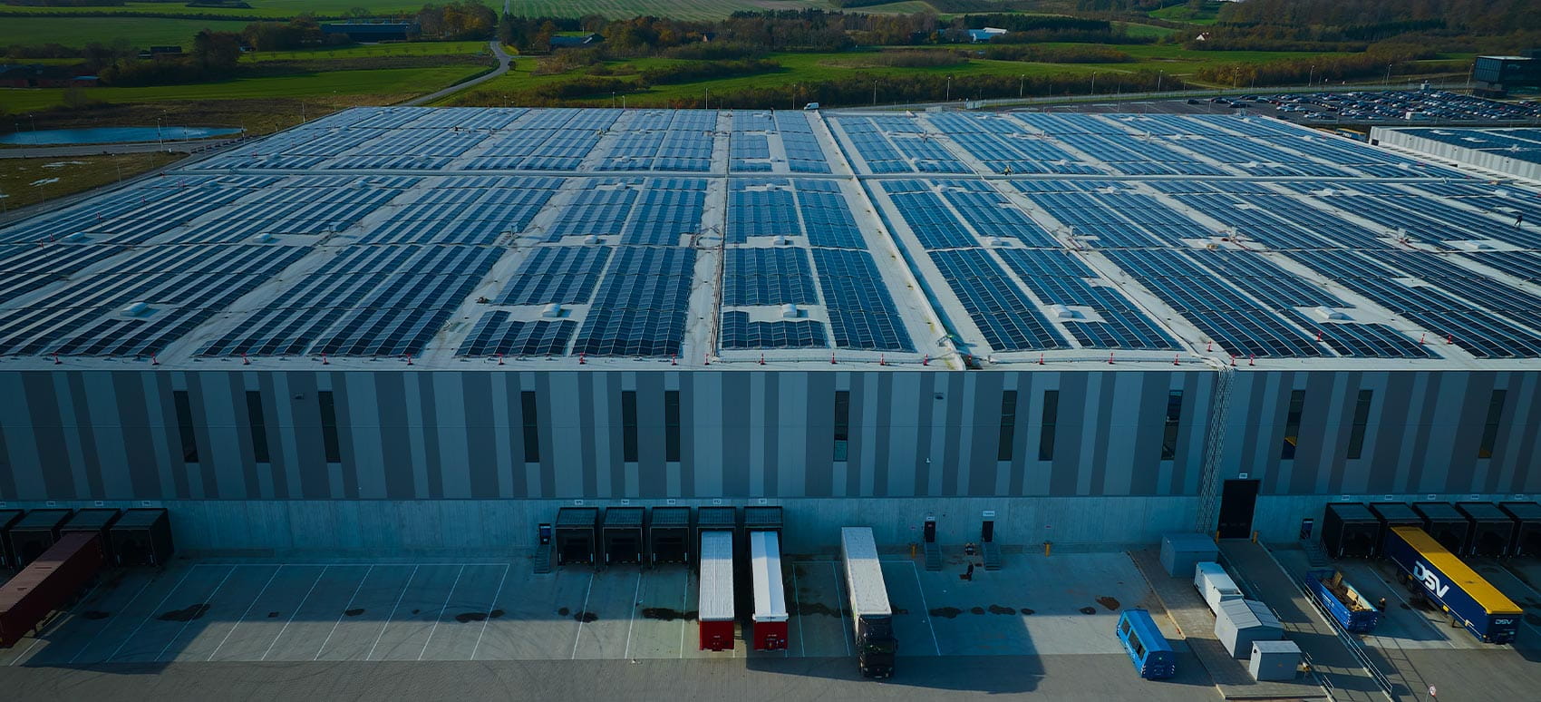 dsv_road_market_report_may_2025_background_1700x774: A large warehouse with solar panels and parked trucks is seen from above.