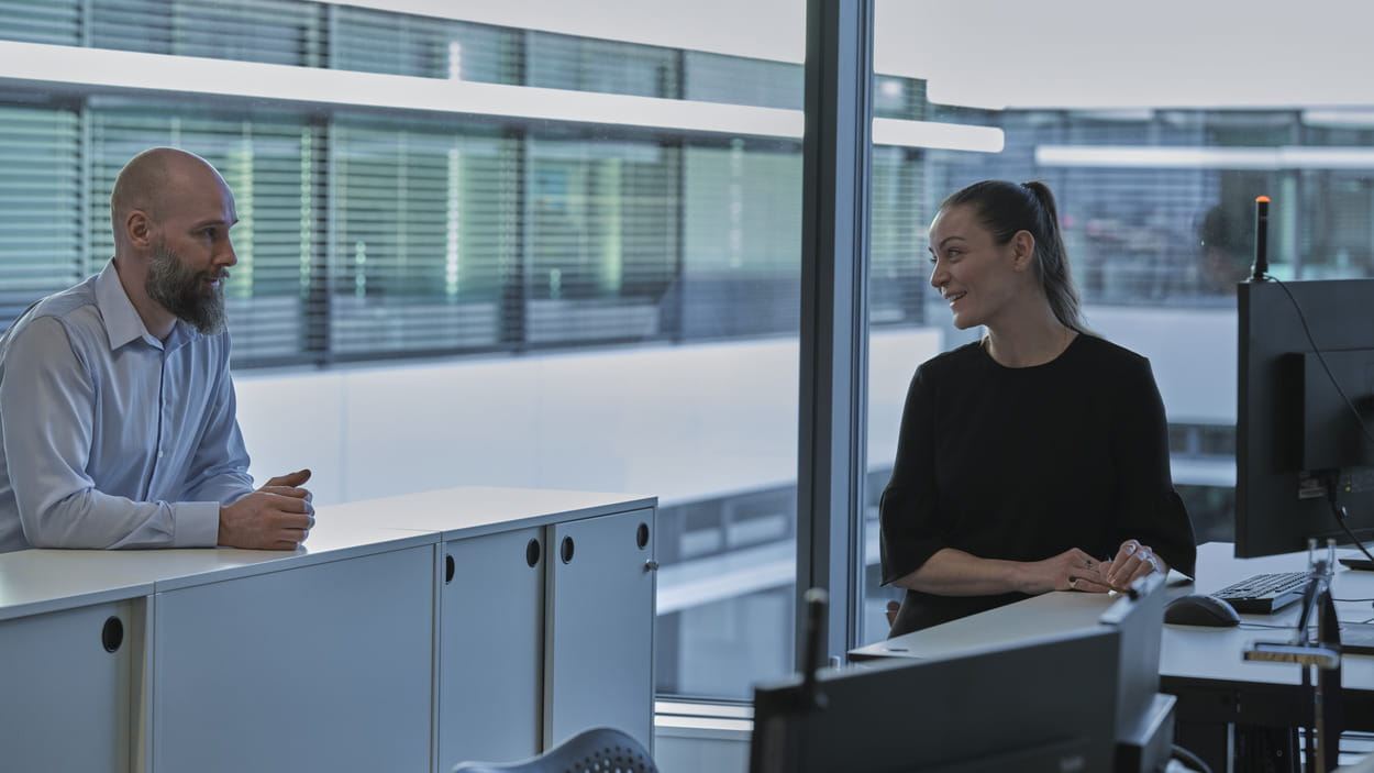 A man and a woman are engaged in conversation in a modern office setting.