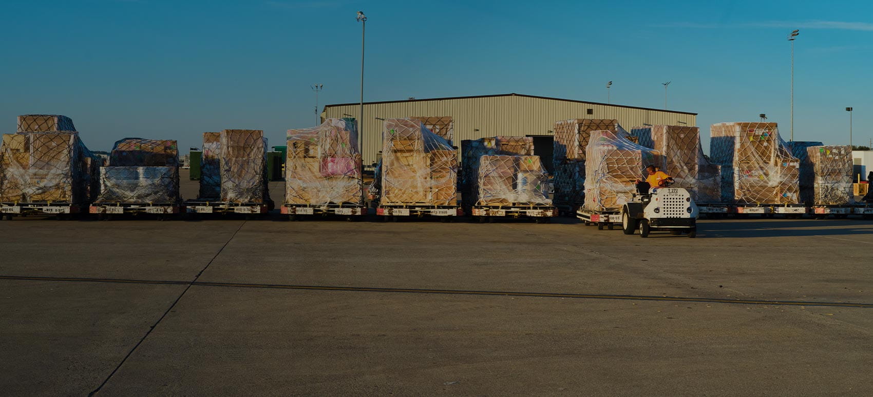 A line of palletized cargo on dollies awaits transport at an airport.