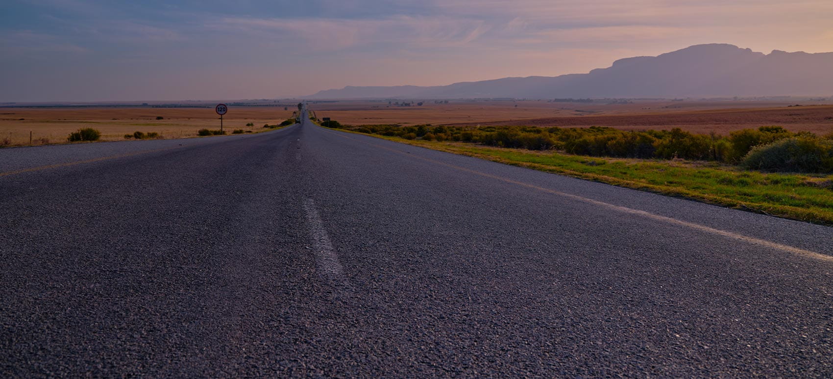 Straight road across open plains toward distant mountains.