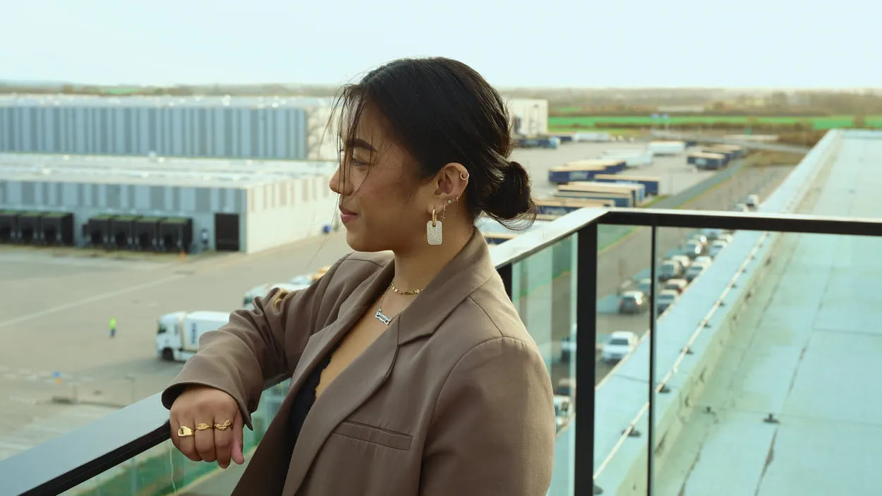  A woman in a brown jacket overlooks a logistics facility with parked vehicles.